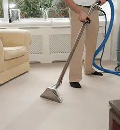 Professional carpet cleaner using a hot-water extraction wand and hose machine in a living room in Fort Lauderdale, FL.