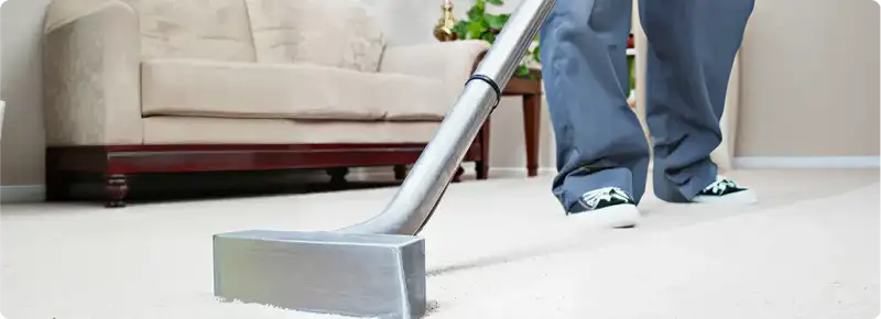 Carpet cleaning technician using a hot-water extraction wand on a light-colored carpet in a living room, Fort Lauderdale, FL.