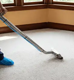 Steam carpet cleaning technician using a hot-water extraction wand on a residential carpet, wearing blue protective shoe covers Fort Lauderdale, FL.