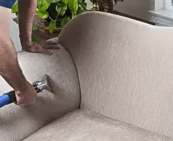 Professional upholstery cleaner deep-cleaning a fabric sofa with a handheld extraction tool and hose in Fort Lauderdale, FL.